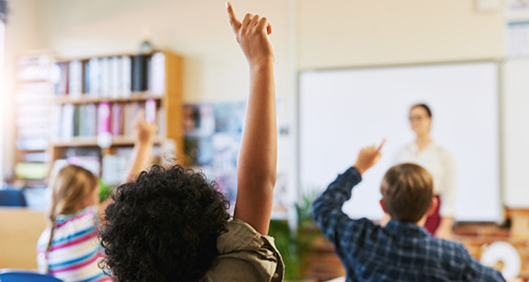 Elementary school students raising hands to answer a question in the classroom